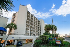 A multi-story hotel with a parking garage, palm trees, and a clear sky.