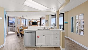 A spacious kitchen with a dishwasher, a dining area with chairs, and a large window providing natural light.