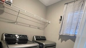 A laundry area with two stainless steel washers and dryers, a white ceiling shelf, and a door with a white curtain.