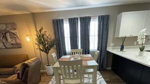 A dining area with a marble-patterned rug, wooden chairs, a table, and a potted plant.