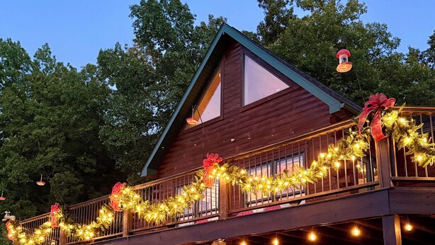 A wooden cabin with a balcony decorated with lights and garlands, a bicycle, and a barbecue grill. - Secluded 5-Bedroom Lodge with Private Lake – Perfect for Large Groups! (Perryville)
