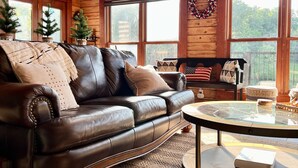 A cozy cabin interior with a leather sofa, a glass coffee table, and a large window with a wreath. - Secluded 5-Bedroom Lodge with Private Lake – Perfect for Large Groups! (Perryville)