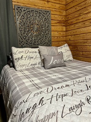 Ein Bett mit einer grau-weißen karierten Tagesdecke und Kissen mit motivierenden Sprüchen.