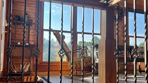 A wooden interior with a view of the outside through large windows, a wooden bench, and a decorative metal railing. - Secluded 5-Bedroom Lodge with Private Lake – Perfect for Large Groups! (Perryville)