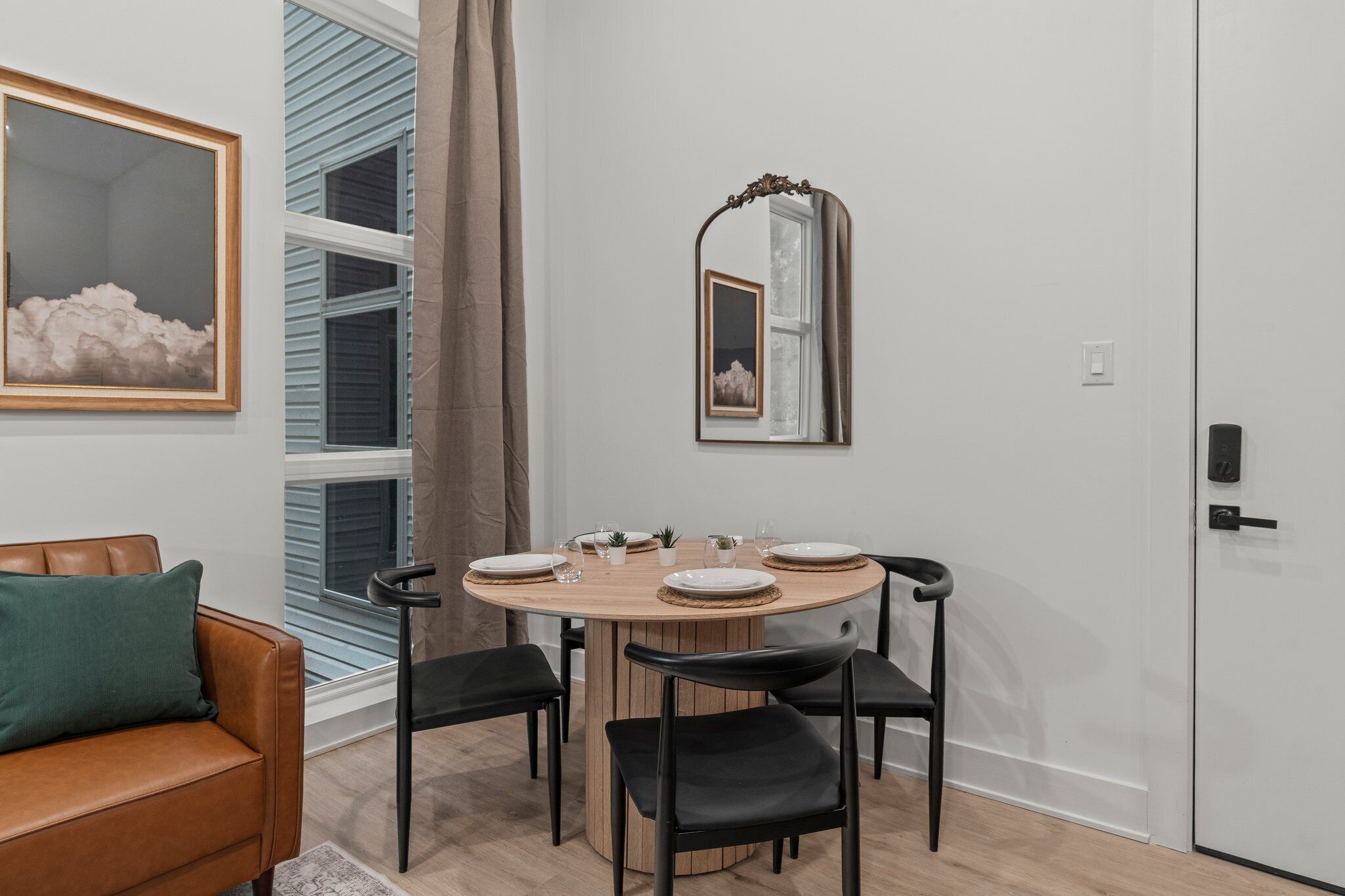A dining area with a round wooden table, black chairs, and a mirror above it.