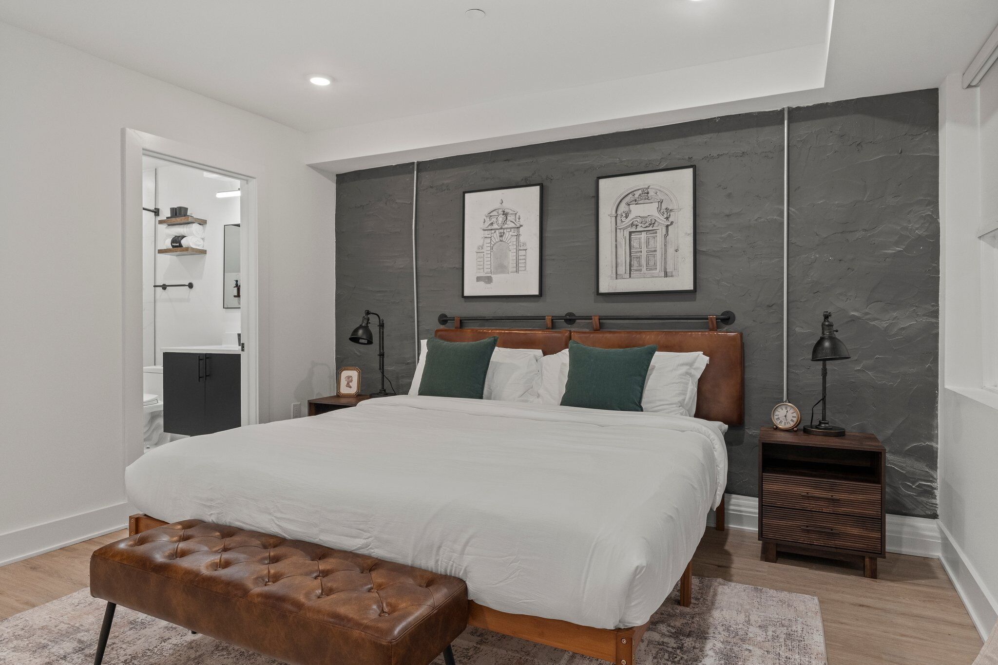A modern bedroom with a large bed, a wooden bench, and two nightstands with lamps.