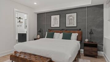 A modern bedroom with a large bed, a wooden bench, and two nightstands with lamps.