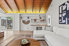 Uma sala de estar moderna com um sofá seccional, uma mesa de centro e uma área de jantar com teto de madeira.