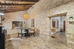 A stone-walled room with a round table and chairs, a hanging light fixture, and a wooden bench.