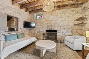 Quarto rústico com paredes de pedra, lareira, cama, sofá e televisão.
