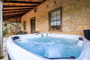 A hot tub in a stone-walled outdoor area with a wooden roof, a bench, and a window. - Baron's Creek Ranch | Big Groups | 3 Homes (Fredericksburg)
