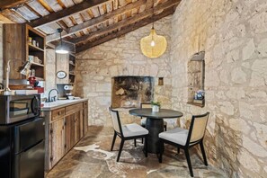 A rustic kitchen with stone walls, a wooden ceiling, and a round dining table with chairs. - Baron's Creek Ranch | Big Groups | 3 Homes (Fredericksburg)