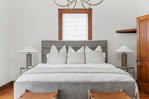 A bedroom with a bed, two bedside tables, a nightstand, a window, and a door. - Baron's Creek Ranch | Big Groups | 3 Homes (Fredericksburg)