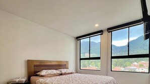 A bedroom with a large bed, a nightstand, a window with a mountain view, and a ceiling fan. - Welcome to your perfect getaway in the heart of Bogota (Bogotá)