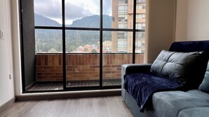 A modern living room with a sliding glass door leading to a balcony, a grey sofa, and a wooden floor. - Welcome to your perfect getaway in the heart of Bogota (Bogotá)