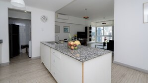 Une cuisine moderne dotée d’un plan de travail en granit, de meubles blancs, d’un évier encastré et d’un panier à fruits.