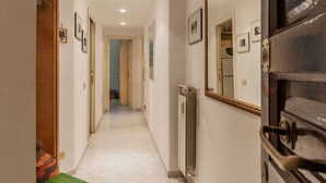 Um corredor com radiador, quadros nas paredes e uma porta de madeira à direita.