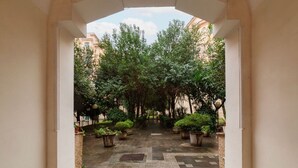 Um pátio com piso de azulejos, plantas em vasos e árvores.