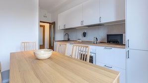 Une cuisine moderne avec des meubles blancs, une table à manger en bois et un grand saladier.