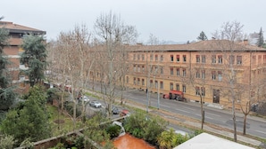 Un immeuble à plusieurs étages avec une façade rouge, une rue devant et des arbres au premier plan.