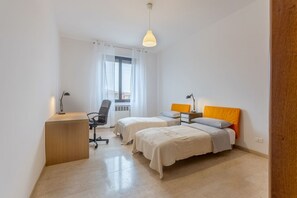 A bedroom with two beds, a desk, a chair, and a window with curtains.