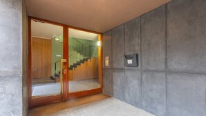 Un couloir avec une porte en bois donnant sur un escalier, un mur gris et un luminaire.