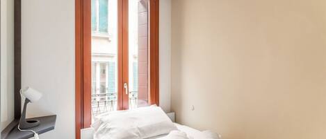 Une chambre d’hôtel avec un lit, un bureau doté d’une lampe, une fenêtre donnant sur des immeubles et une paire de serviettes sur le lit.