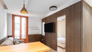 Ein modernes Zimmer mit einem Holztisch, einer Couch, einem an der Wand befestigten Fernseher und einem Balkon mit Geländer.