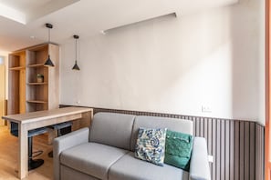 A modern living room with a grey sofa, a wooden table, and a hanging pendant light.