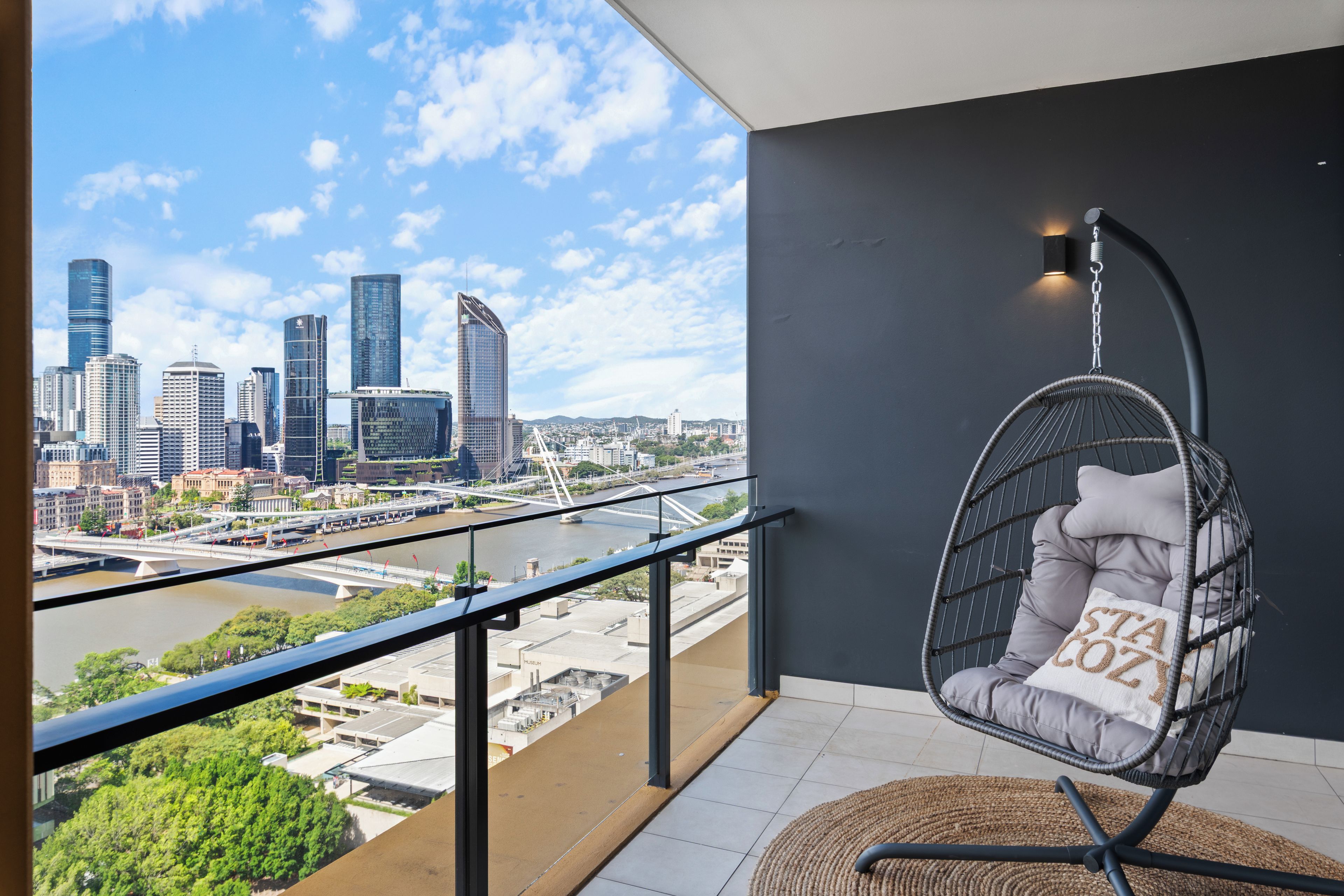 A balcony with a hanging chair, a view of a city skyline, and a river.