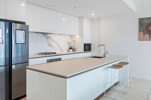 Cozinha moderna com ilha central, eletrodomésticos de aço inoxidável e armários brancos.
