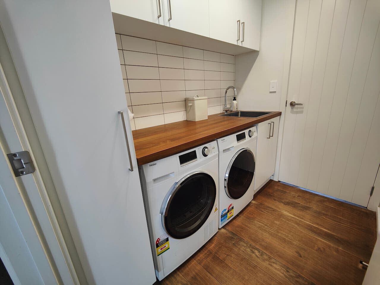 Un lavadero con dos lavadoras de carga frontal, una encimera de madera y un revoque de azulejos.