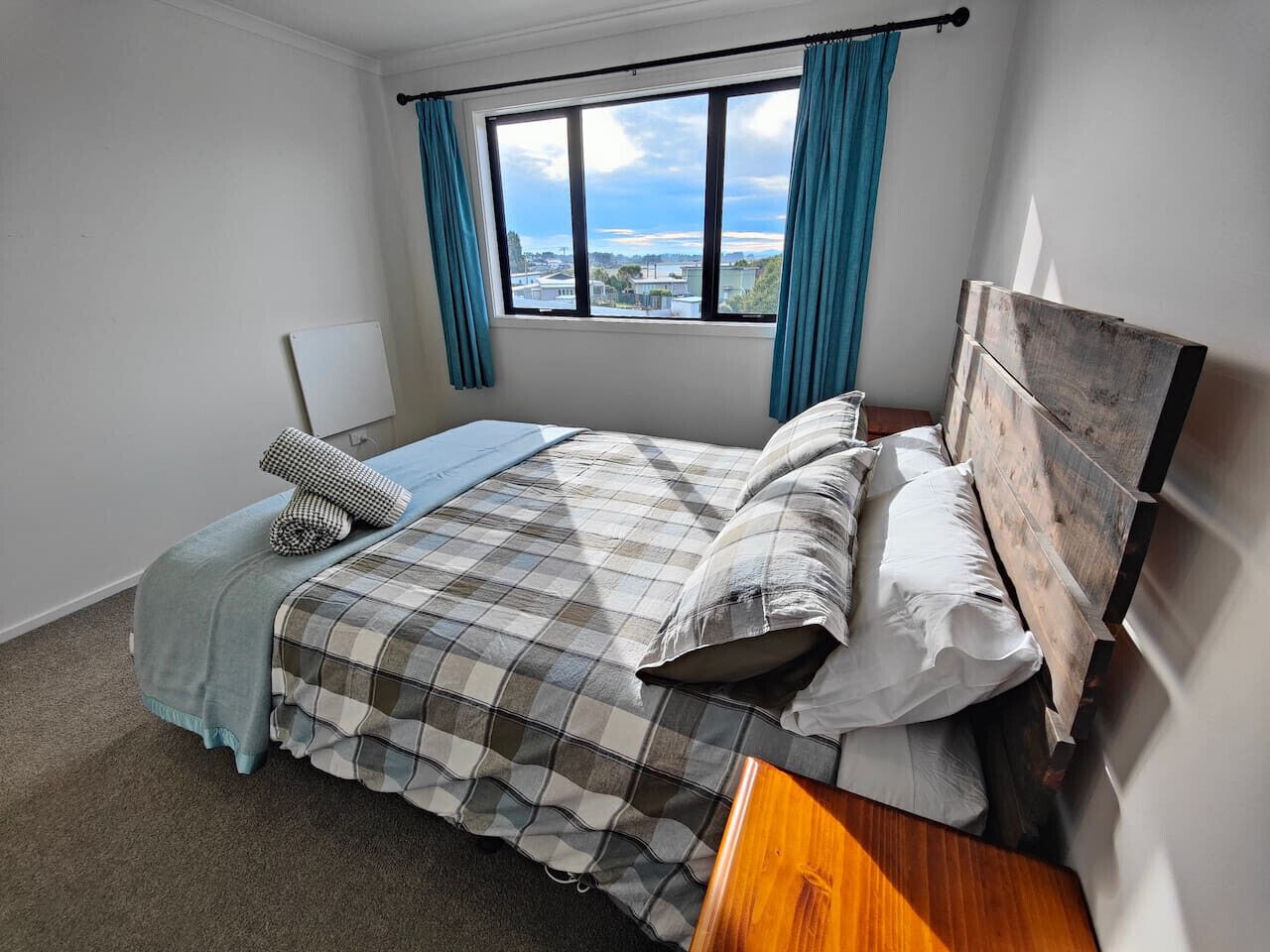 Ein Schlafzimmer mit großem Fenster, einem Bett mit kariertem Überwurf und Blick auf Gebäude.