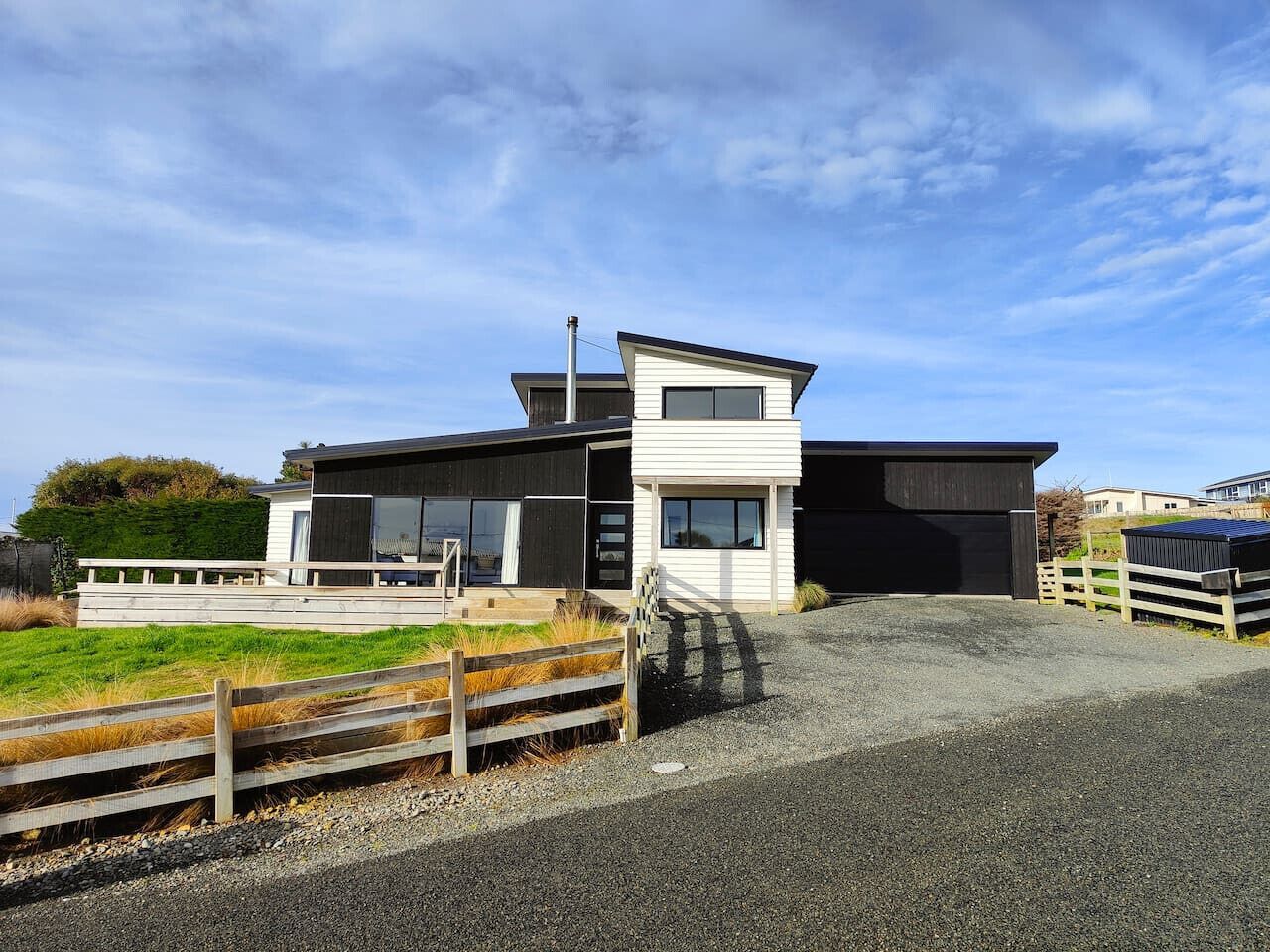 A modern two-story building with a flat roof, large windows, and a gravel driveway.