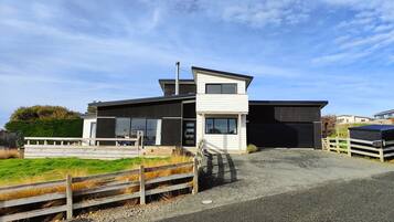 A modern two-story building with a flat roof, large windows, and a gravel driveway.