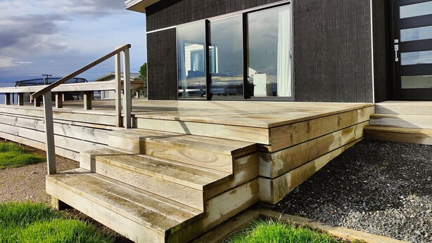 A modern building with a wooden deck and steps leading to a glass door. - Riverton Luxury in the Lane (Riverton / Aparima)