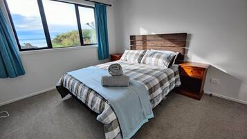 A bedroom with a large window, a bed with plaid bedding, a wooden headboard, and a nightstand.