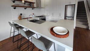 A modern kitchen with a central island, bar stools, pendant lighting, and stainless steel appliances. - Riverton Luxury in the Lane (Riverton / Aparima)