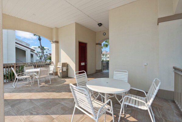 A covered outdoor patio with white metal furniture, a clock on the wall, and a view of the surrounding buildings.
