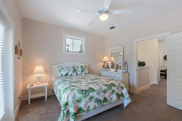 A bedroom with a bed, bedside lamps, a ceiling fan, a window with blinds, and a mirror.