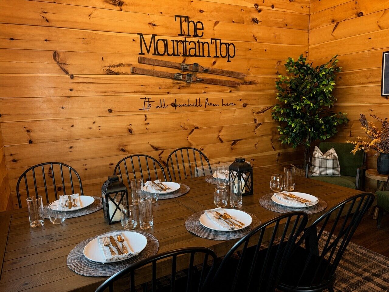 A wooden dining room with a table set for six, chairs, a plant, and a sign reading 'The Mountain Top'.