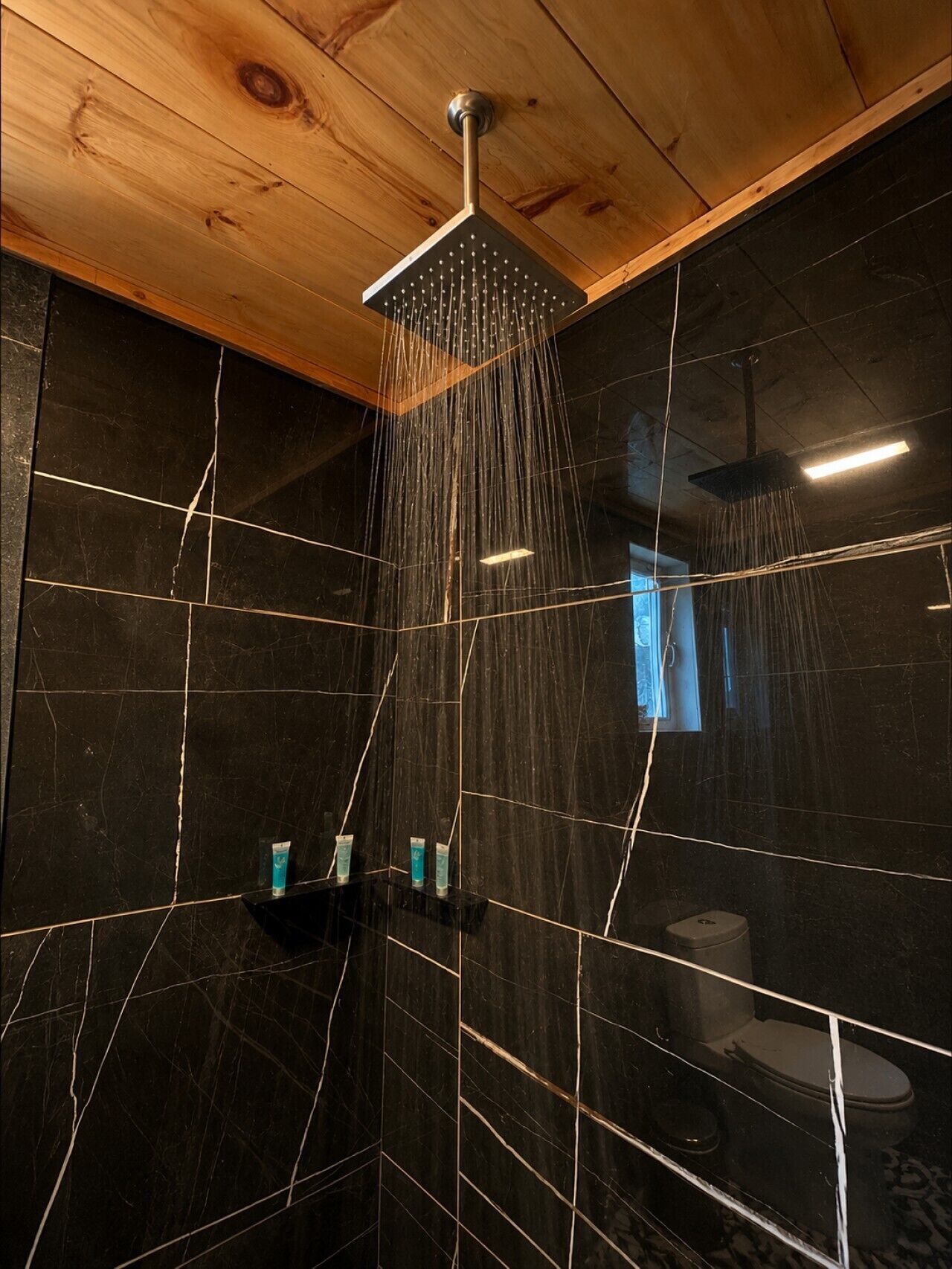 A shower with a modern design, a wooden ceiling, and black marble walls.