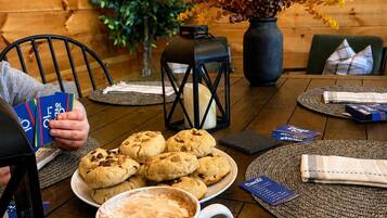 Un ambiente interno accogliente con pareti in legno, un tavolo con biscotti e una tazza di caffè, e una pianta con foglie autunnali.
