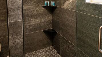 Un espace douche moderne avec des carreaux de couleur sombre, une pomme de douche et une étagère contenant des articles de toilette.