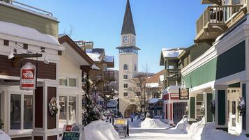 Une rue enneigée bordée d’immeubles, avec un beffroi et une enseigne indiquant « The North Face Summit Shop ».