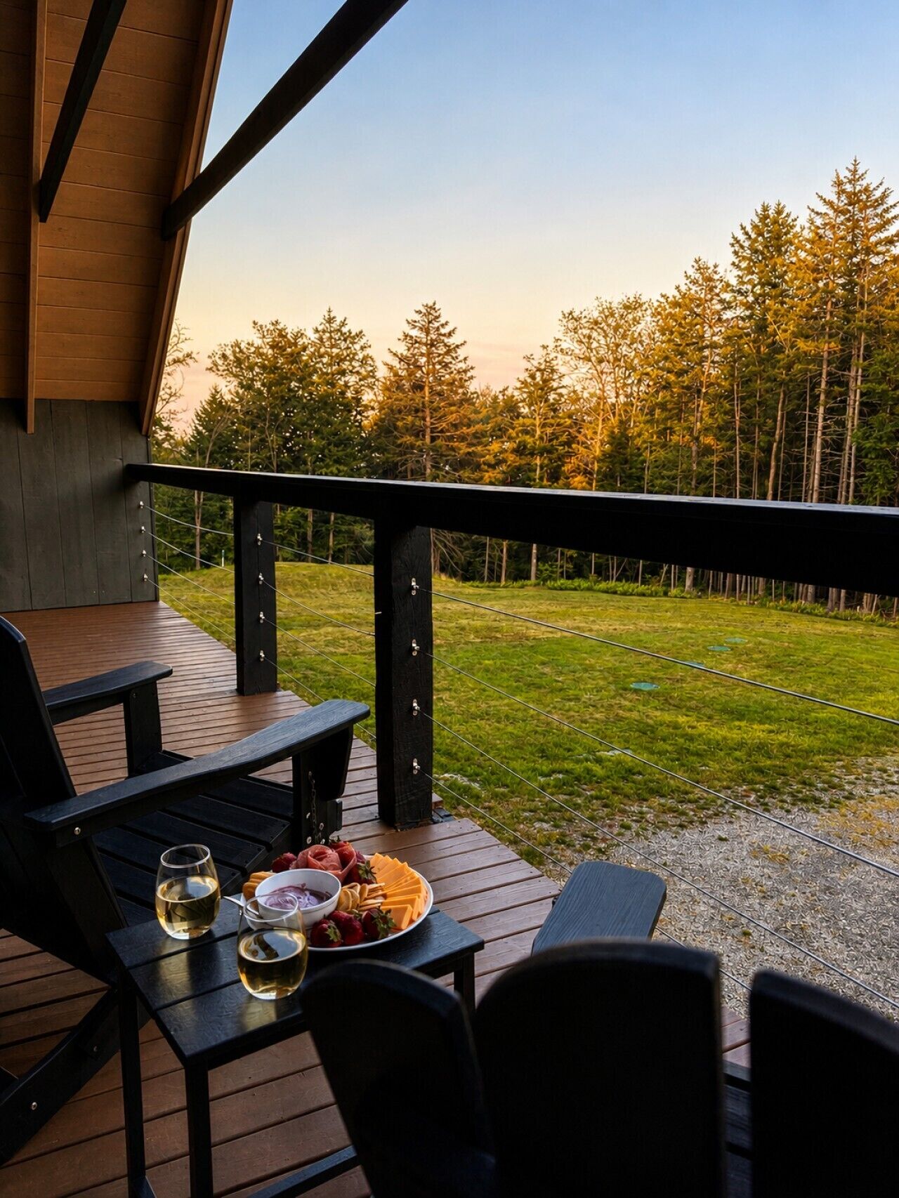 A wooden deck with a table set for dining, overlooking a grassy area with trees.