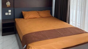 A modern hotel room with a large bed, dark headboard, and a nightstand with a lamp. - Laika Homestay (Banguntapan)