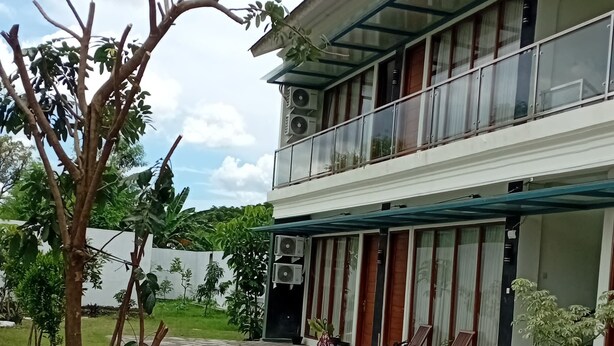 A two-story building with a balcony, a paved walkway, and potted plants. - Laika Homestay (Banguntapan)