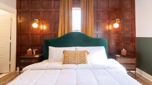A neatly made bed with white linens and a green headboard, flanked by wooden nightstands with lamps.