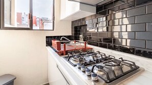 A modern kitchen with a gas stove, black tiled backsplash, and a window overlooking a cityscape. - Amazing Apartment in Condesa (Ciudad de México)